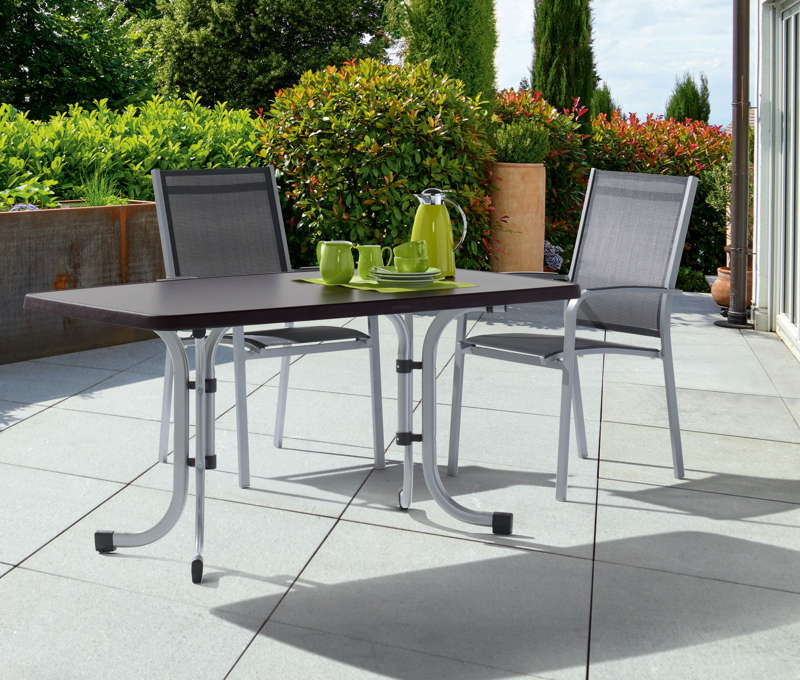 Klapptisch in Graphit auf einer Terrasse mit zwei Stühlen, von vorne betrachtet.