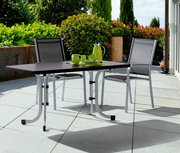 Klapptisch in Graphit auf einer Terrasse mit zwei Stühlen, von vorne betrachtet.