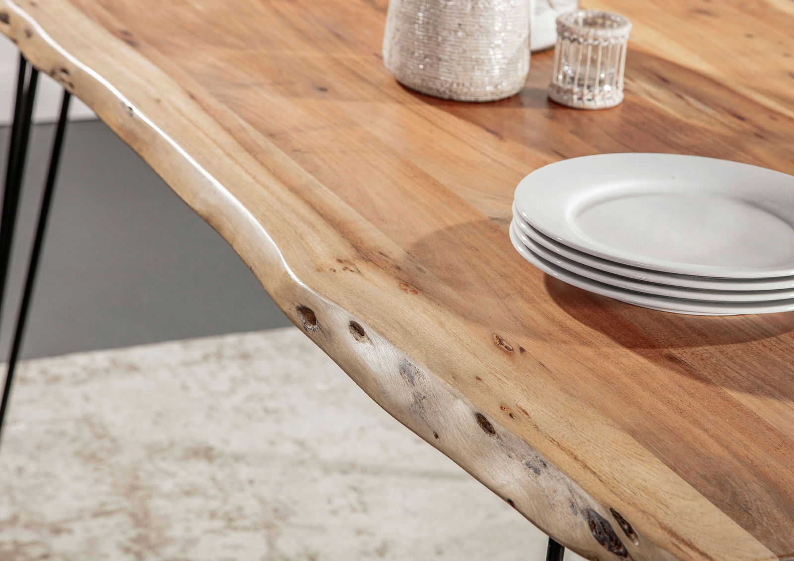 Nahaufnahme eines Esstisches mit natürlicher Holzmaserung und unregelmäßiger Kante, von oben betrachtet. Auf dem Tisch stehen weiße Teller und dekorative Objekte.