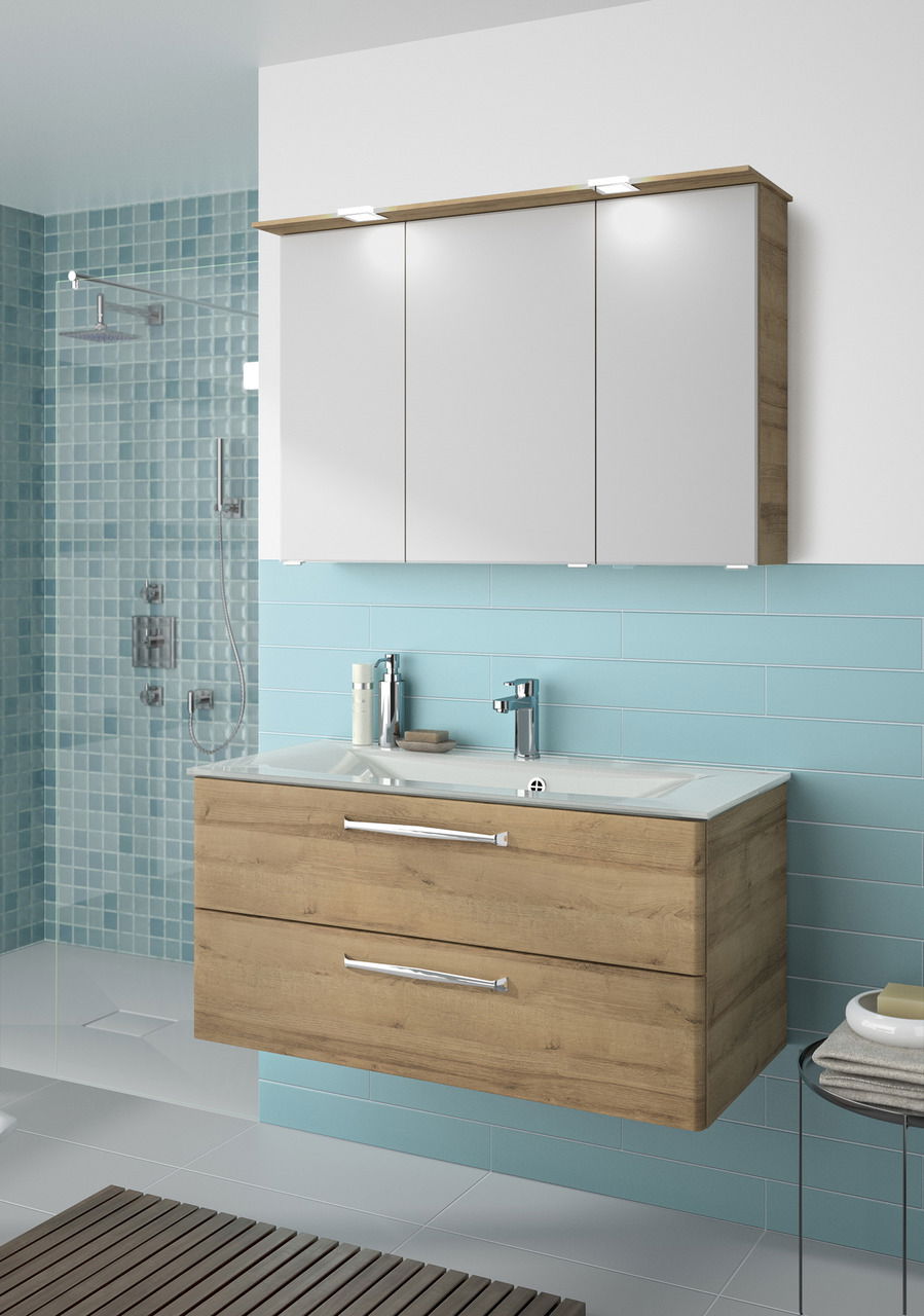 Pelipal Badblock TRENTINO Moderner Badblock mit Holzoptik und weißen Schranktüren, frontal betrachtet in einem stilvollen Badezimmer mit blauen Fliesen.