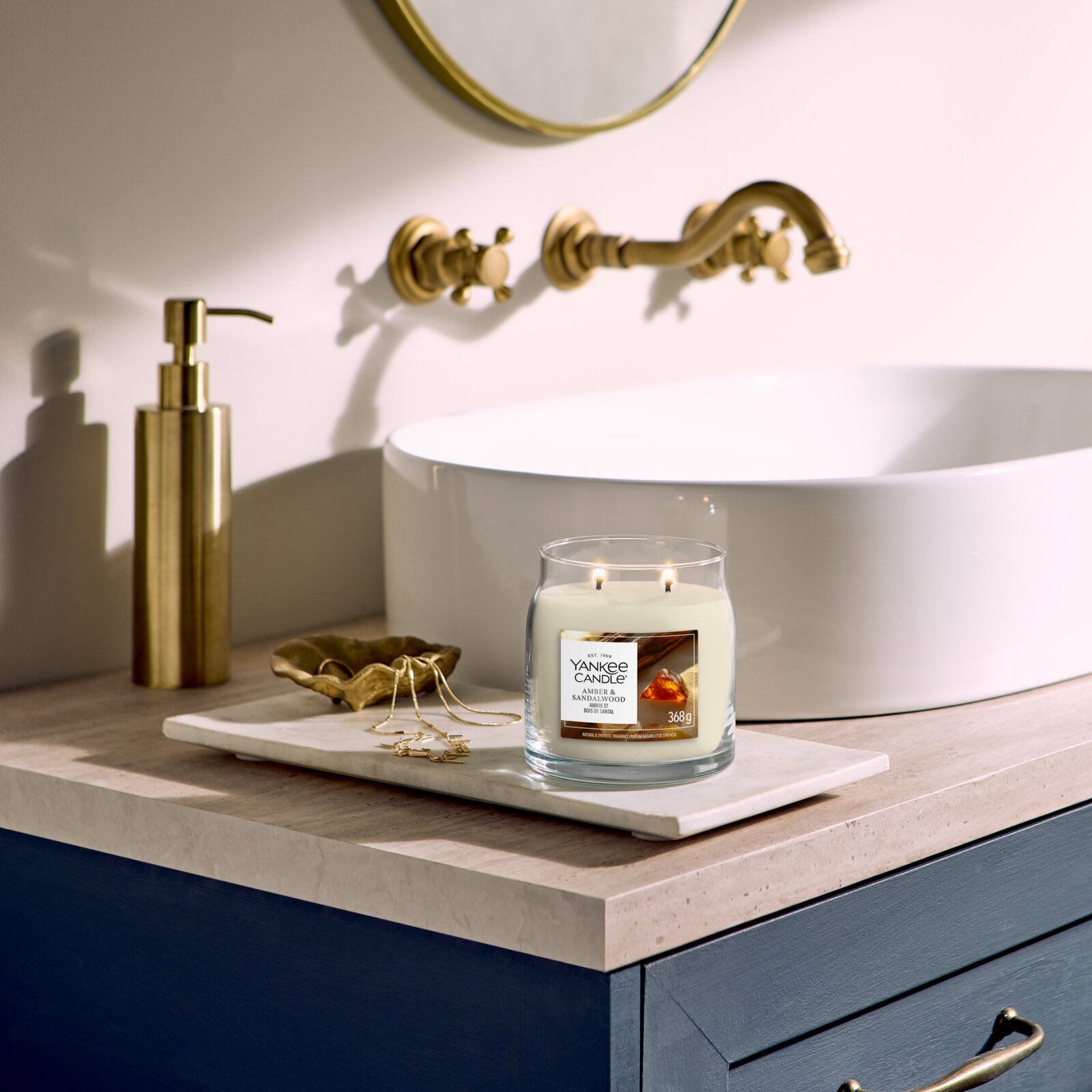 Yankee Candle Duftkerze Amber & Sandalwood im Glas mit zwei brennenden Dochten, frontal aus leicht erhöhter Perspektive auf einem eleganten Badezimmer-Waschtisch inszeniert