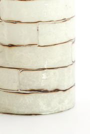 Nahaufnahme eines Teelichthalters mit einem strukturierten, cremefarbenen Keramikdesign in Ziegeloptik.