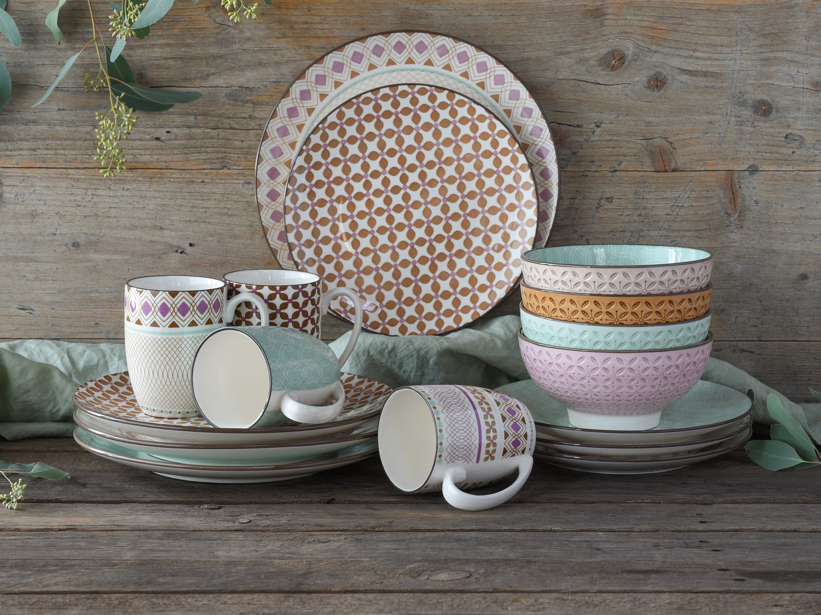Kombiservice 16-tlg mit bunten Mustern, bestehend aus Tellern, Tassen und Schalen, auf rustikalem Holztisch aus seitlicher Perspektive.