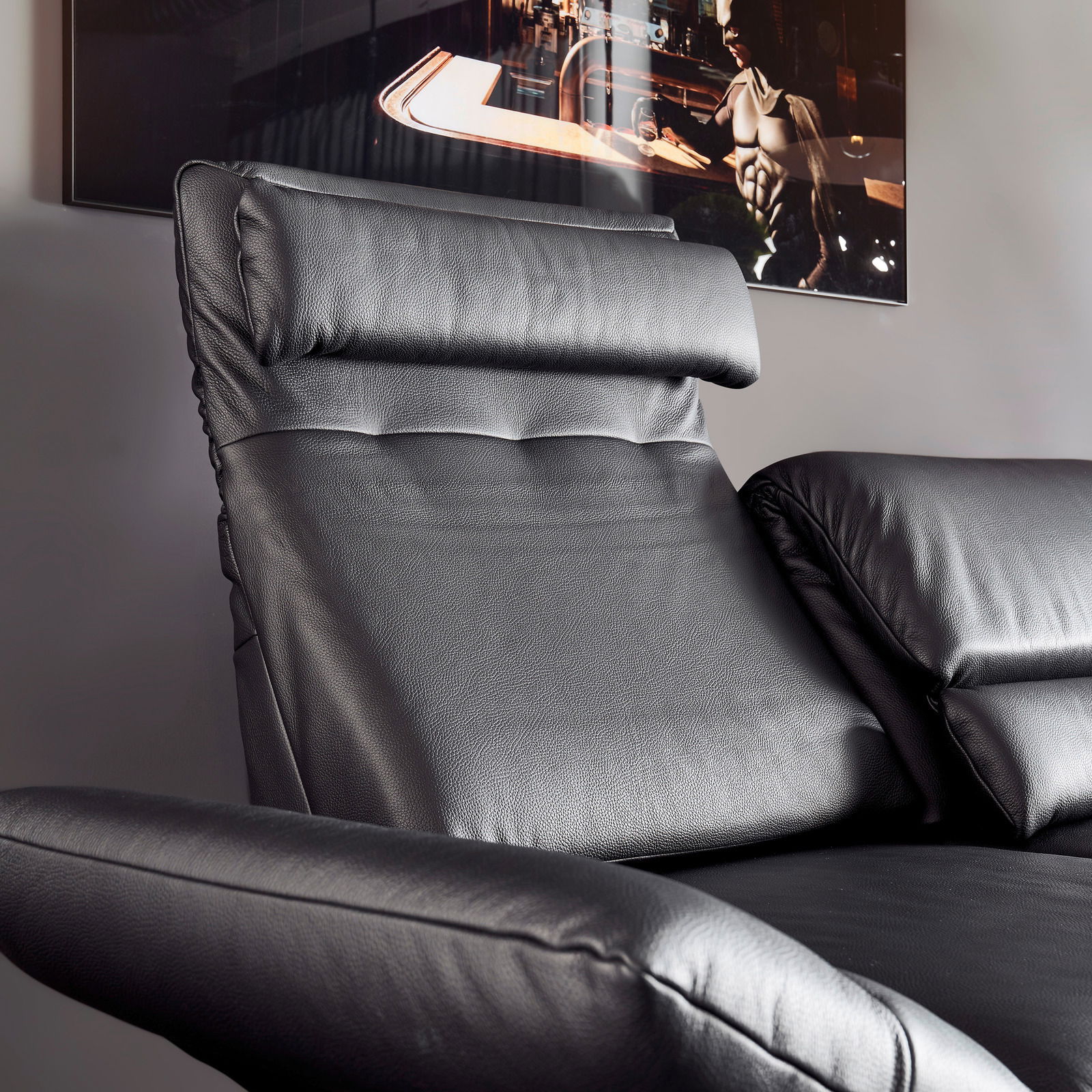 Nahaufnahme eines schwarzen Ledersofas mit verstellbarer Kopfstütze und Armlehne, seitliche Perspektive