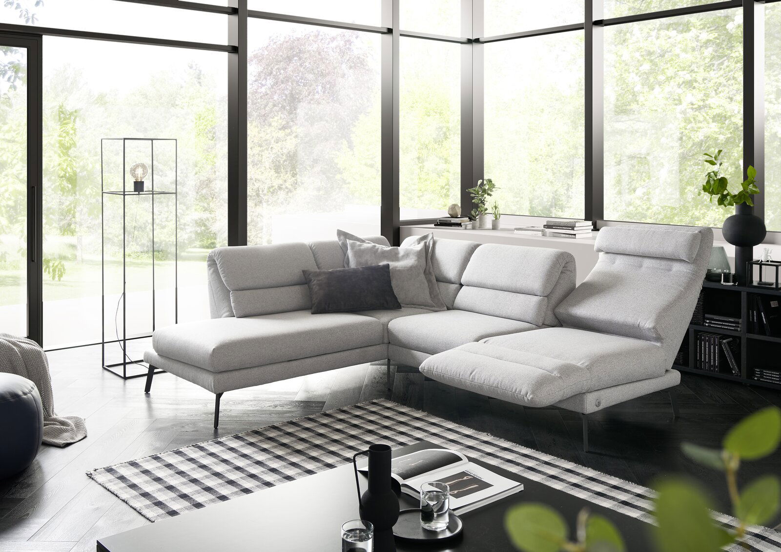 Moderne graue Eckgarnitur in einem hellen Wohnzimmer mit großen Fenstern, seitliche Perspektive