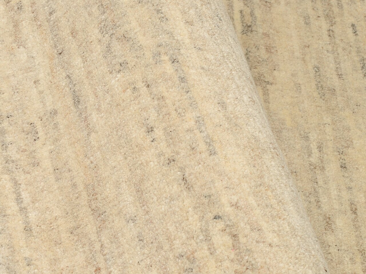 Nahaufnahme eines beigen Wollteppichs mit dezenter Musterung, leicht von der Seite fotografiert.