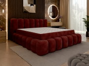Een gestoffeerd bed in een moderne slaapkamer, gezien vanaf de zijkant, met een rood, gestoffeerd frame en hoofdeinde, omringd door stijlvolle decoratie.