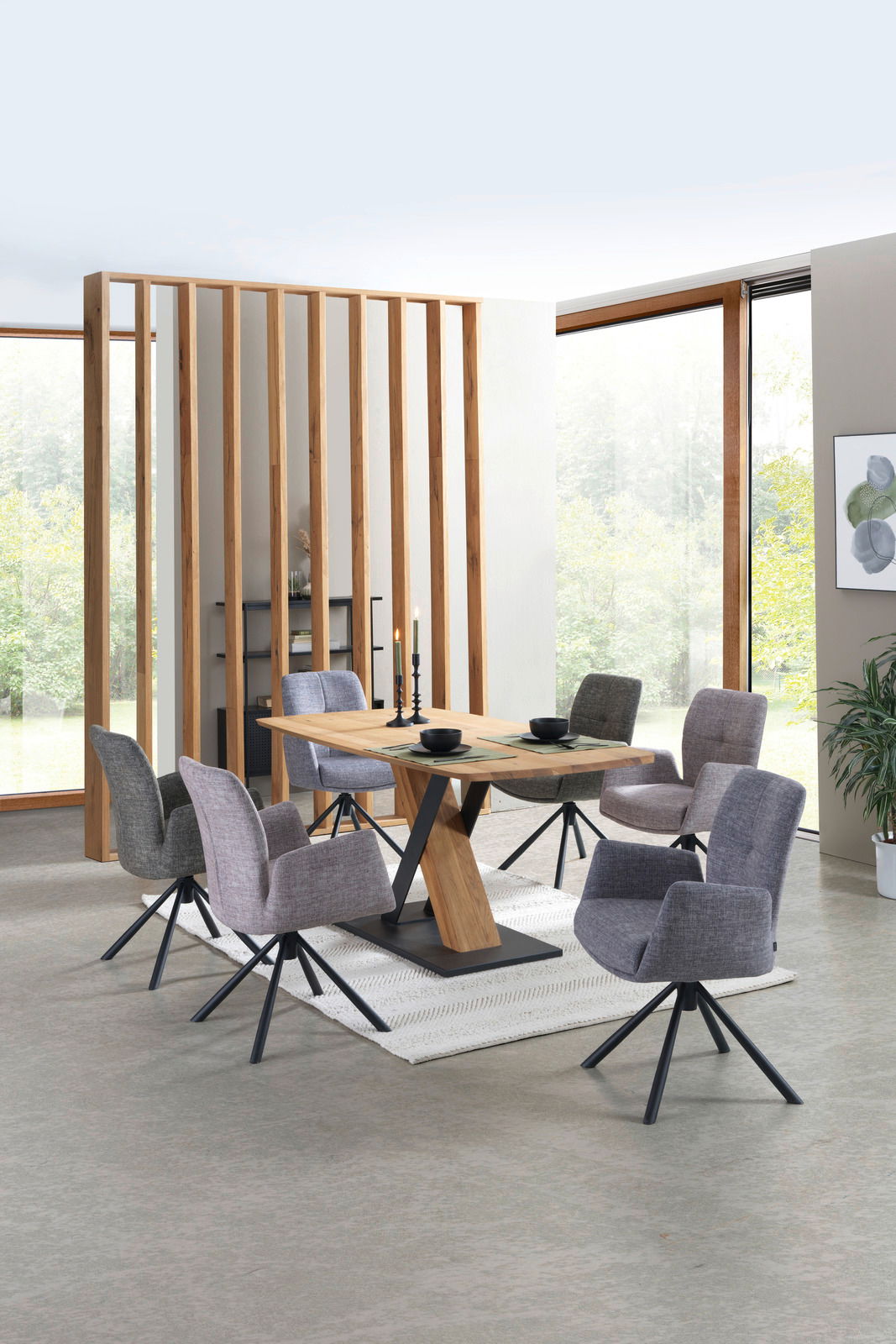 Moderner Esstisch aus Holz mit schwarzem Metallgestell, umgeben von sechs grauen Stühlen in einem hellen Raum mit großen Fenstern, aus seitlicher Perspektive.