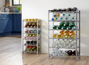 Zwei silberne Flaschenregale aus Metall mit mehreren Ebenen, befüllt mit Wein- und Wasserflaschen, in einer hellen Küche vor weißer Wand; Perspektive: frontale Ansicht auf Augenhöhe, leicht schräg von links.