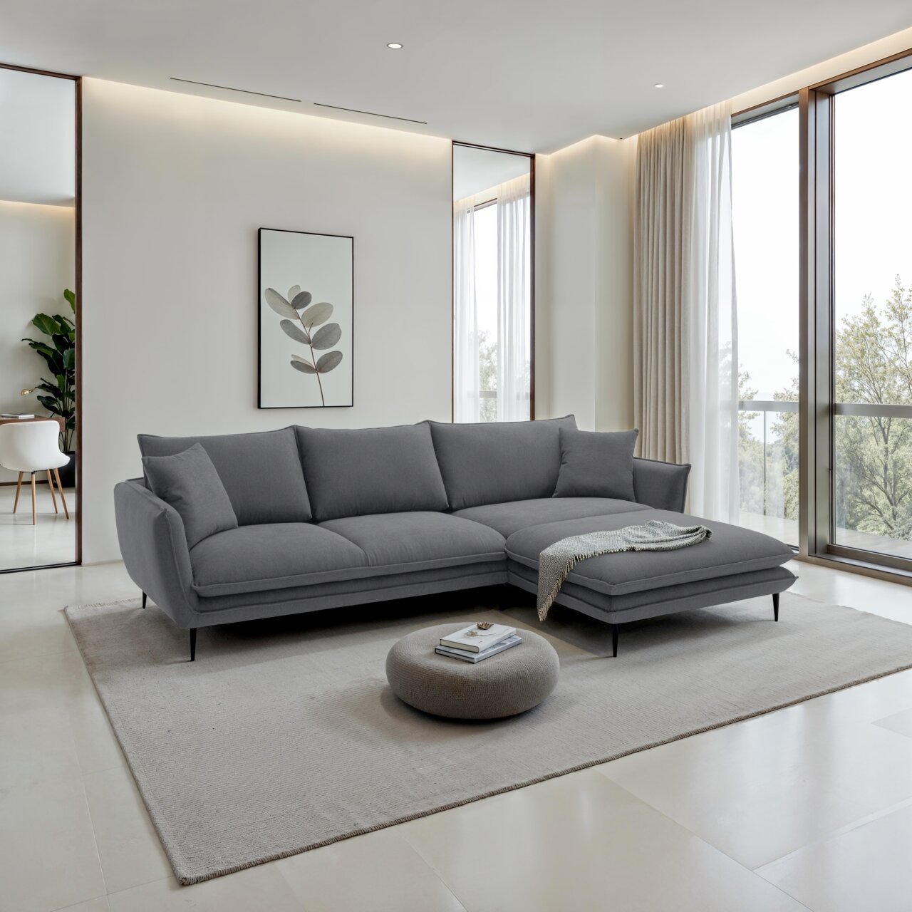 Modernes graues L-förmiges Ecksofa mit Recamiere und schwarzen Metallfüßen im hellen Wohnzimmer, frontale leicht seitliche Perspektive von links; auf hellem Teppich mit rundem Pouf und großen Fensterfronten