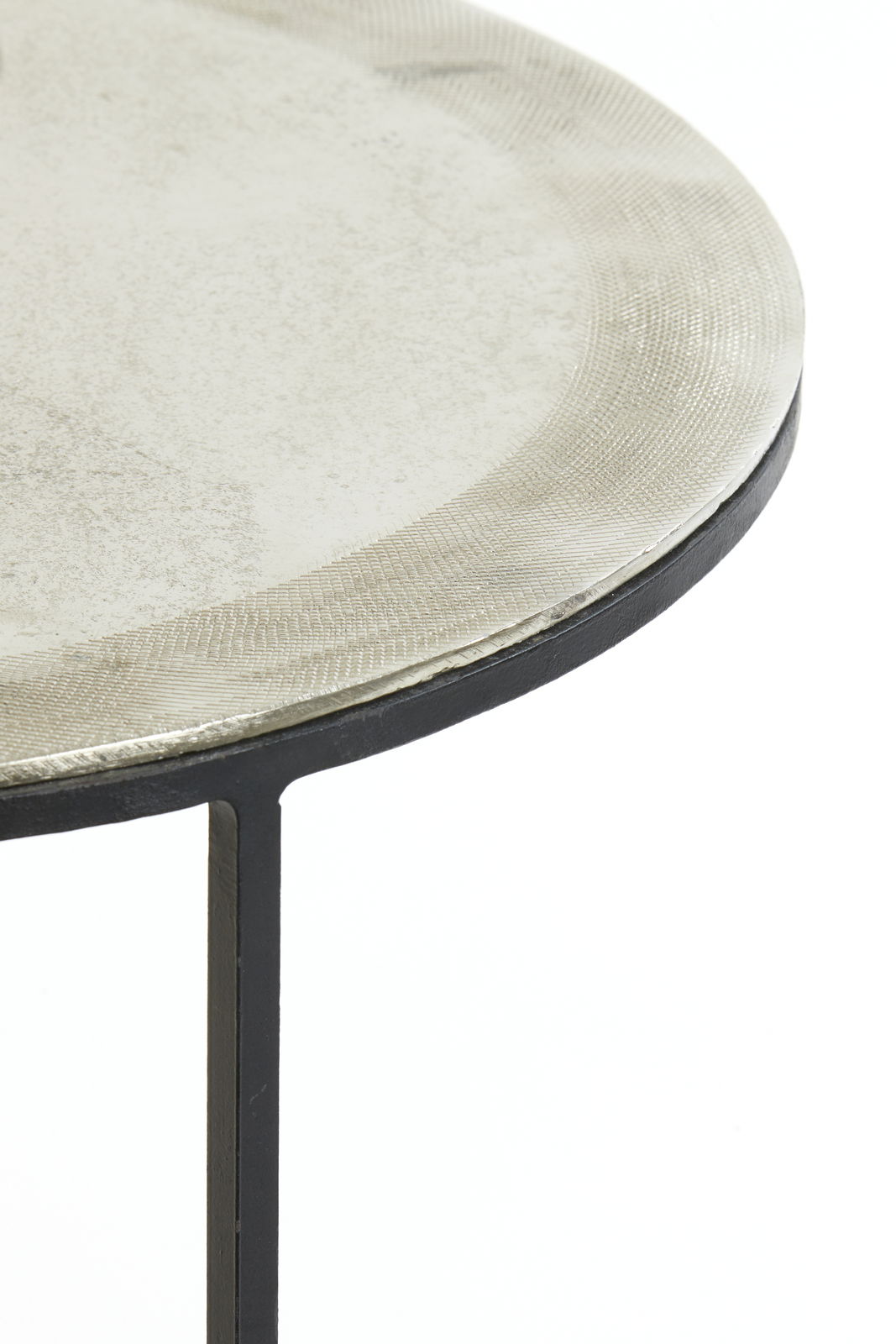 Nahaufnahme eines runden Beistelltisches mit metallischer Oberfläche und schwarzem Gestell, seitliche Perspektive.