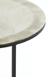 Nahaufnahme eines runden Beistelltisches mit metallischer Oberfläche und schwarzem Gestell, seitliche Perspektive.