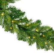 Detailaanzicht van een volle groene kunstkerstslinger met warmwitte ledverlichting, schuin van voren gefotografeerd tegen een witte achtergrond