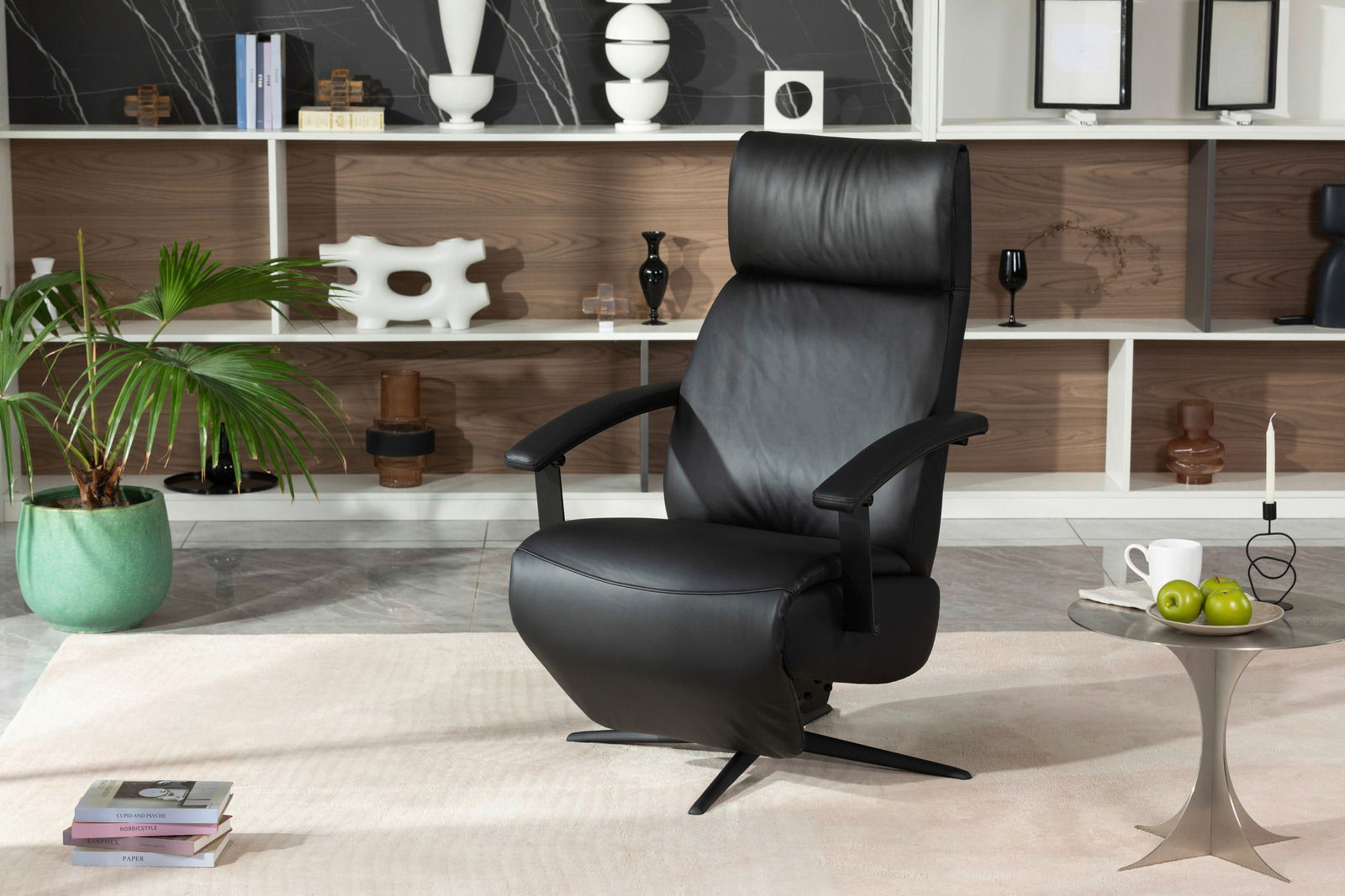 XORA Relaxsessel MAX 2.0 Schwarzer Relaxsessel aus Leder in einem modernen Wohnzimmer, frontal fotografiert. Im Hintergrund ein Regal mit Dekorationen und eine grüne Pflanze.