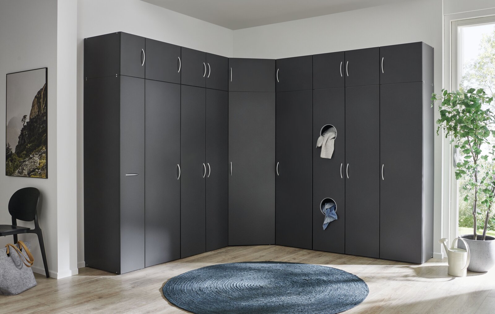 Eckschrank in dunklem Design, perspektivisch von vorne links fotografiert, mit mehreren Türen und runden Öffnungen für Kleidung.