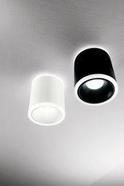 Zwei zylindrische LED-Aufbauspots, einer in Weiß und einer in Schwarz, an der Decke montiert, aus der Perspektive von unten betrachtet.