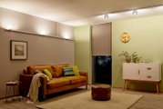 Wohnzimmer mit moderner Beleuchtung, die an der Decke entlang verläuft, mit einem Flexverbinder für URAIL-System. Perspektive von der Seite des Raumes mit Sofa, Beistelltisch und Kommode.