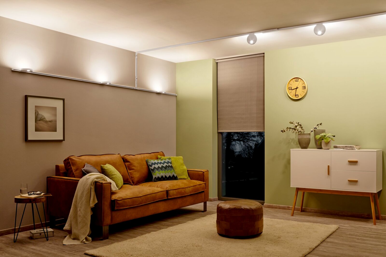 Wohnzimmer mit moderner Beleuchtung, die an der Decke entlang verläuft, mit einem Flexverbinder für URAIL-System. Perspektive von der Seite des Raumes mit Sofa, Beistelltisch und Kommode.