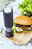 Elektrische Pfeffer- oder Salzmühle in schwarzem Design, stehend auf einem Holzbrett neben einem Burger, aus seitlicher Perspektive fotografiert.