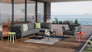 Moderner Beistelltisch auf einer Terrasse mit Meerblick, umgeben von stilvollen Gartenmöbeln. Perspektive von vorne.