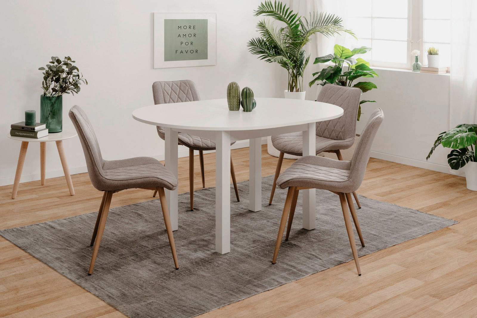 Moderner Esstisch mit weißer, ovaler Tischplatte und vier grauen Stühlen in einem hellen Raum mit Pflanzen, aus seitlicher Perspektive.