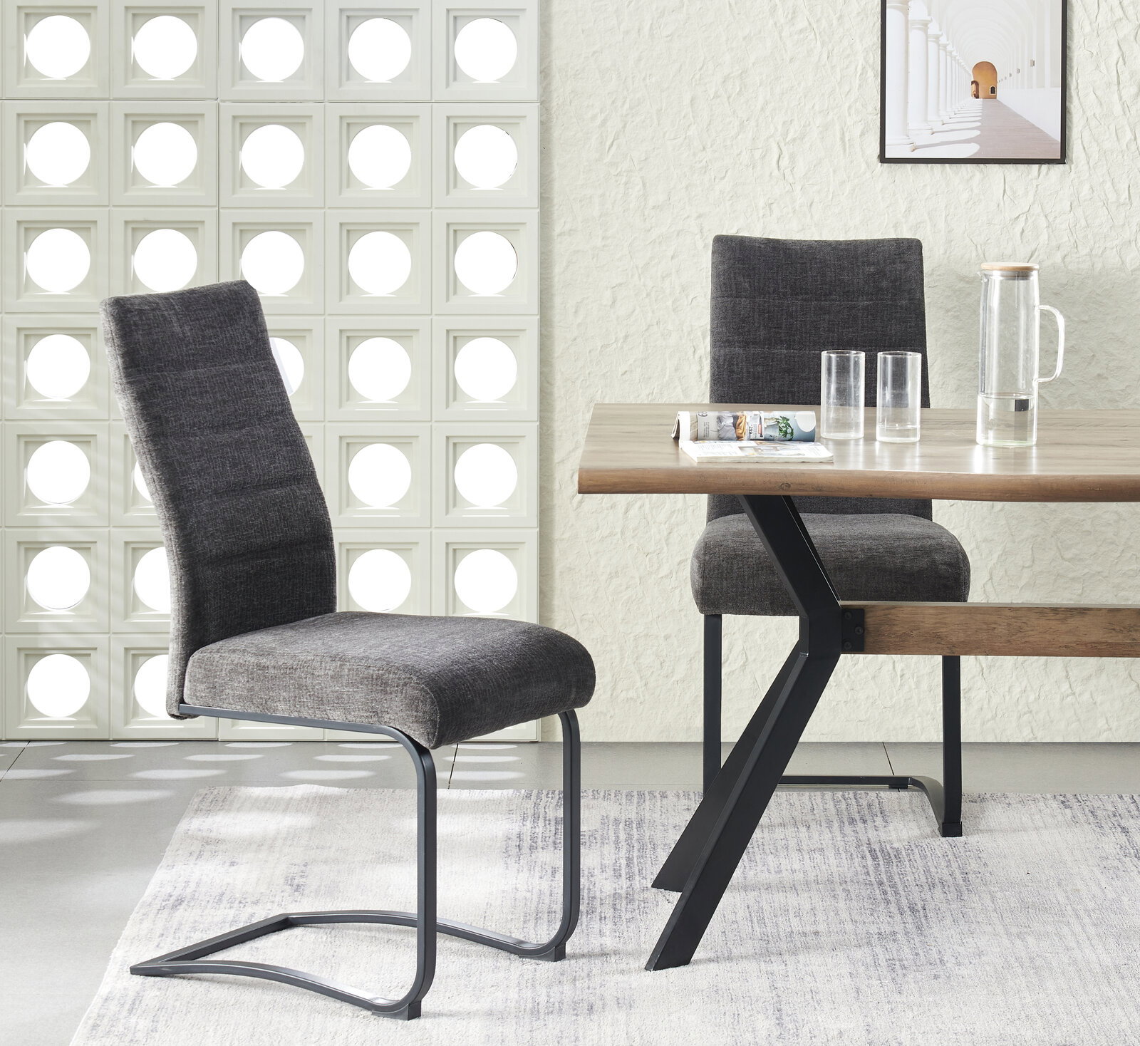 Moderner Esszimmerstuhl mit dunkelgrauem Stoffbezug und schwarzem Freischwinger-Metallgestell, seitliche Perspektive im Wohnambiente neben Holztisch.