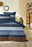 Bettwäsche-Set mit blauen, braunen und weißen Streifen, frontal fotografiert in einem gemütlichen Schlafzimmer.