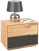 Nachtkonsole aus Holz mit zwei Schubladen, obere Schublade in Holzoptik, untere Schublade in dunklem Grau, darauf eine silberne Lampe und eine Brille auf einem Buch, Perspektive von vorne.