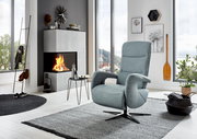 Moderner Relaxsessel in hellblauem Stoff, seitliche Perspektive, in einem stilvollen Wohnzimmer mit Kamin und großen Fenstern.