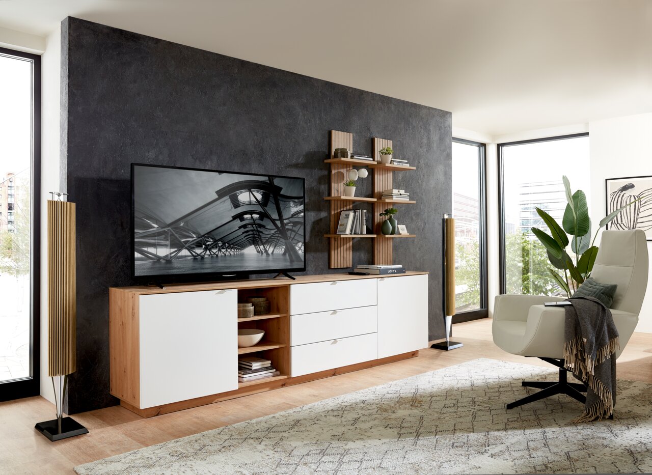 Modernes Wohnzimmer mit einem Wandpaneel in Holzoptik, das als Hintergrund für ein TV-Gerät dient. Perspektive von vorne auf das Wandpaneel und die darauf platzierten Regale mit Dekoration.
