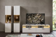 Moderne Wohnzimmeransicht mit zwei weißen Vitrinen und einem TV-Schrank, frontal betrachtet. Die Vitrinen sind mit dekorativen Objekten beleuchtet.