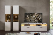 Moderne Wohnzimmeransicht mit zwei weißen Vitrinen und einem TV-Schrank, frontal betrachtet. Die Vitrinen sind mit dekorativen Objekten beleuchtet.