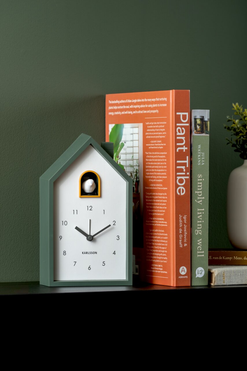 Moderner KARLSSON Wecker in Hausform, grün, auf einem Regal neben Büchern, seitliche Perspektive