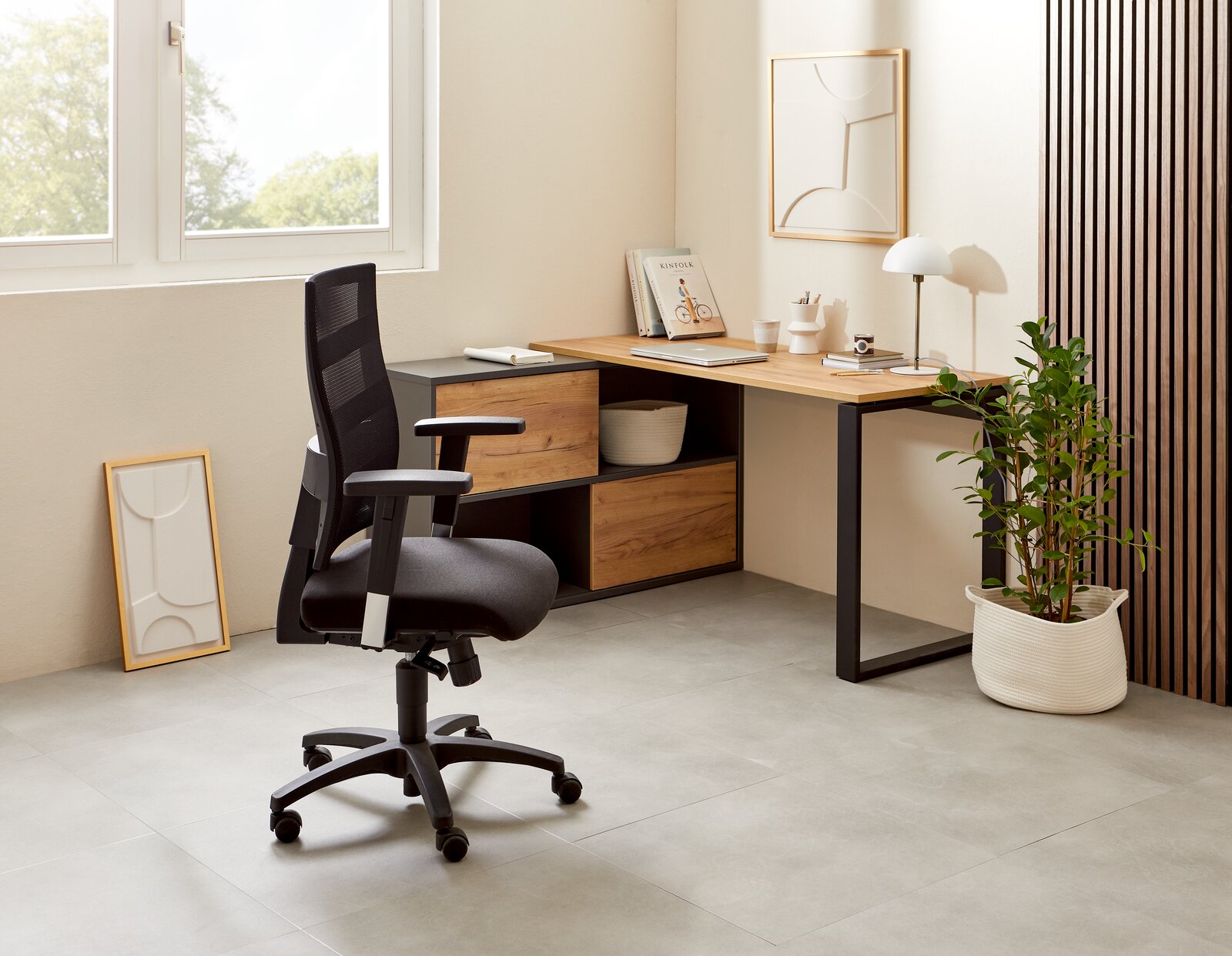 Moderner Winkelschreibtisch RENTON in einem hellen Raum, mit Holz- und Metallelementen, von der Seite betrachtet. Ein ergonomischer Bürostuhl steht davor, umgeben von Dekorationen und Pflanzen.