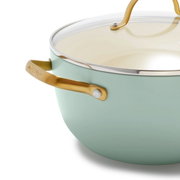 Close-up van een mintgroene kookpan met een goudkleurig handvat en een glazen deksel, gezien vanaf de zijkant.