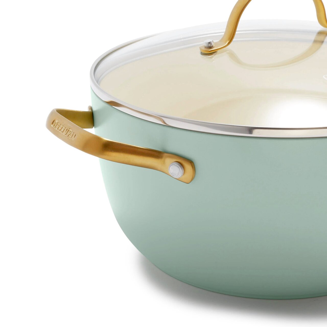 Close-up van een mintgroene kookpan met een goudkleurig handvat en een glazen deksel, gezien vanaf de zijkant.