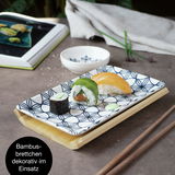 Sushi-Set mit blauem Blumenmuster, bestehend aus einem rechteckigen Teller auf einem Bambusbrettchen, mit Sushi und Essstäbchen, seitliche Perspektive.