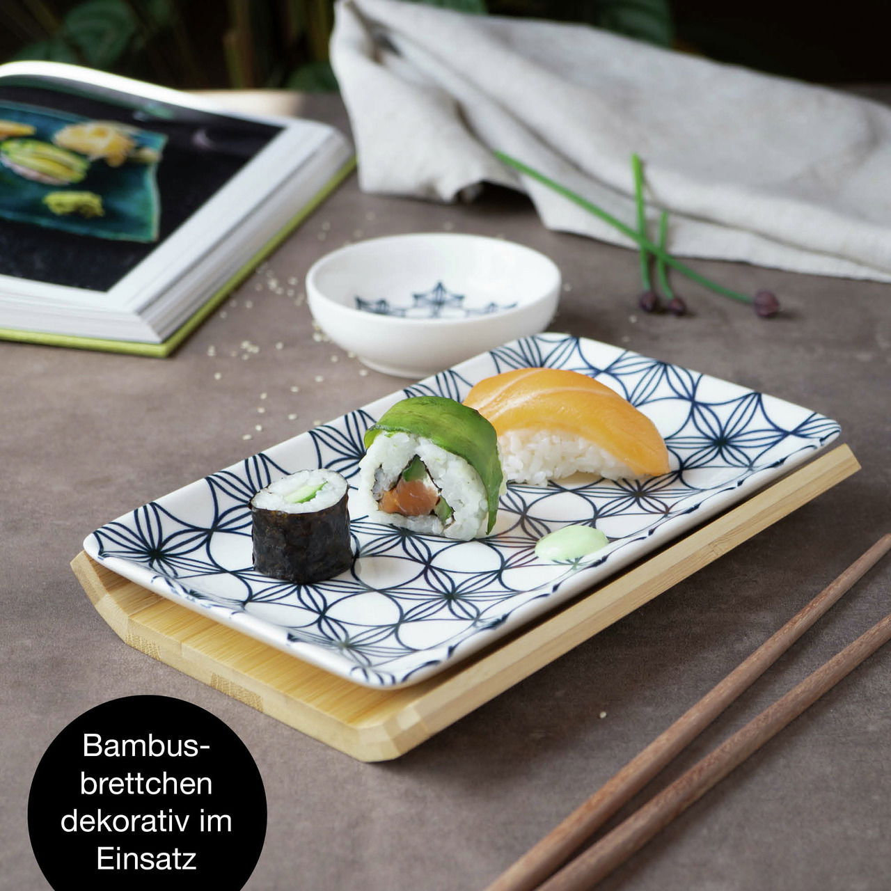 Sushi-Set mit blauem Blumenmuster, bestehend aus einem rechteckigen Teller auf einem Bambusbrettchen, mit Sushi und Essstäbchen, seitliche Perspektive.