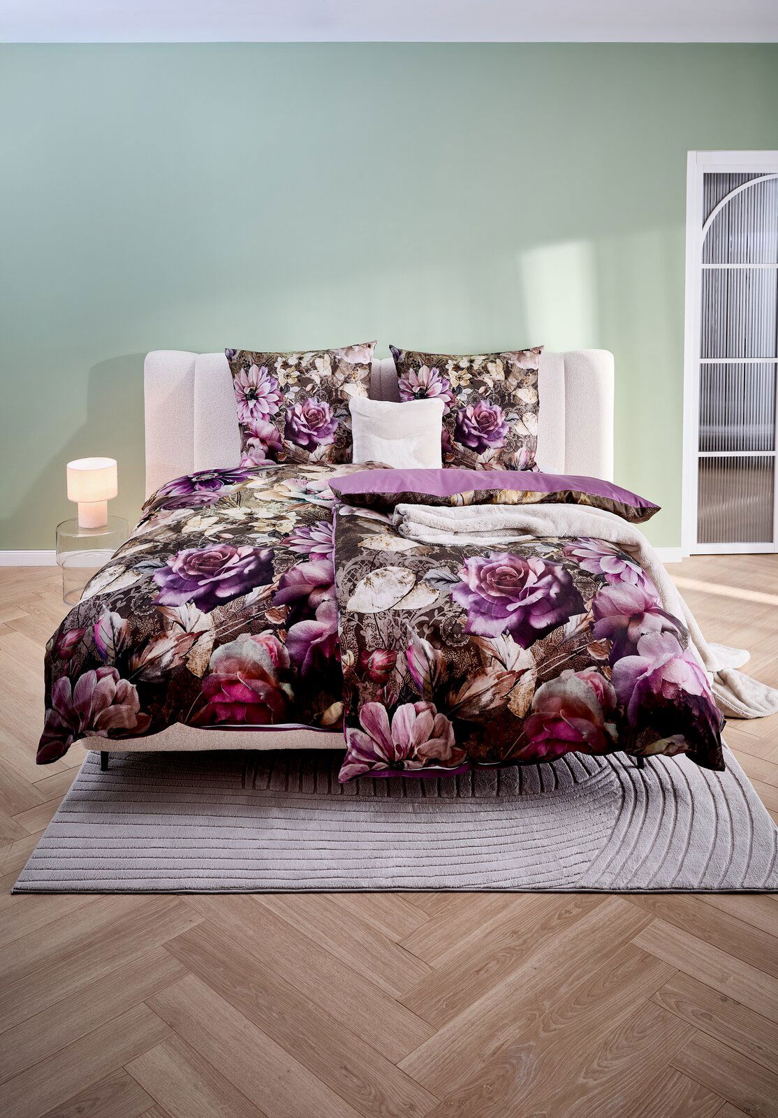 Wendebettwäsche mit floralem Muster in Lila- und Rosatönen, auf einem Bett in einem modern eingerichteten Schlafzimmer, aus der Frontalperspektive fotografiert.