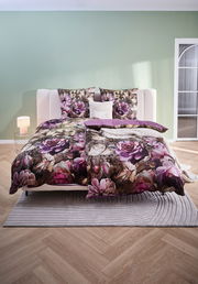 Wendebettwäsche mit floralem Muster in Lila- und Rosatönen, auf einem Bett in einem modern eingerichteten Schlafzimmer, aus der Frontalperspektive fotografiert.