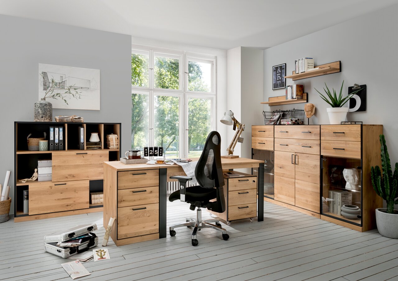 Moderner Schreibtisch aus Holz mit Schubladen, umgeben von Regalen und Schränken in einem hellen Büro mit Blick auf ein großes Fenster.