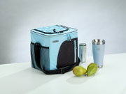 Hellblaue THERMOS-Kühltasche mit schwarzem Schultergurt und Außentaschen, aus schräger Vorderansicht neben Thermobecher, Getränkedose und zwei Birnen präsentiert