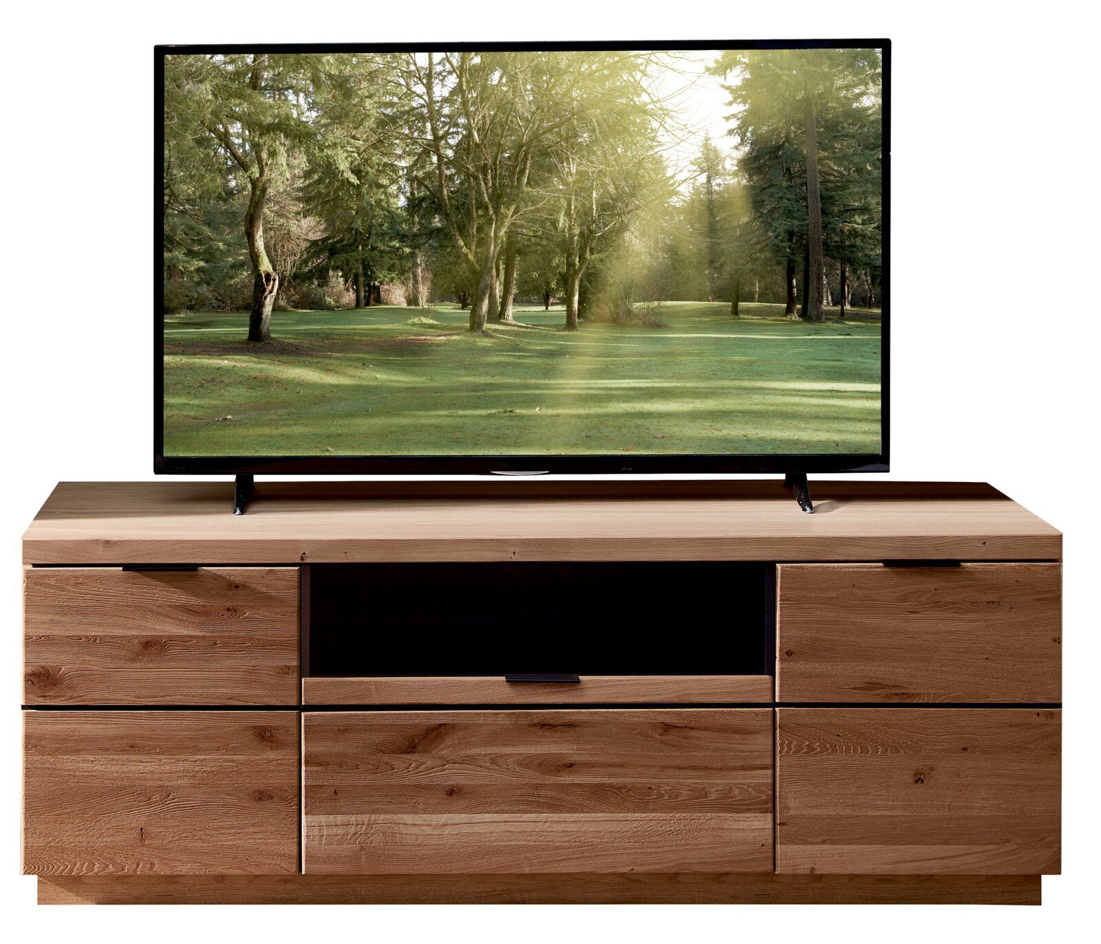 Cantus Lowboard DONNA Frontansicht eines großen Flachbildfernsehers auf einem modernen TV-Lowboard aus hellem Holz mit mehreren Schubladen und offenem Mittelfach; auf dem Bildschirm ist eine sonnige Waldlichtung zu sehen.