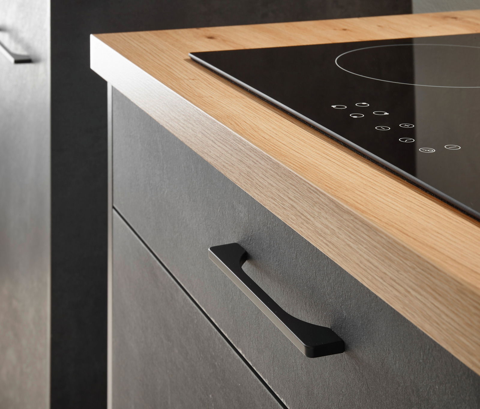 Nahaufnahme eines modernen Küchenblocks mit Holzarbeitsplatte und schwarzem Induktionskochfeld, seitliche Perspektive.