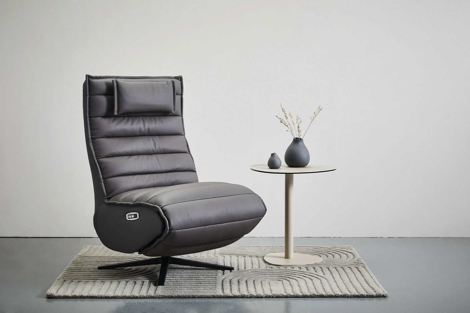 Stylife Relaxliege MARINA Graue Relaxliege mit hohem Rücken und Kopfstütze, seitliche Ansicht, auf einem Teppich neben einem kleinen runden Tisch mit zwei Vasen.