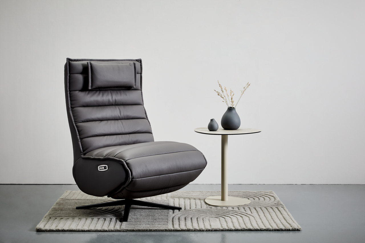 Stylife Relaxliege MARINA Graue Relaxliege mit hohem Rücken und Kopfstütze, seitliche Ansicht, auf einem Teppich neben einem kleinen runden Tisch mit zwei Vasen.