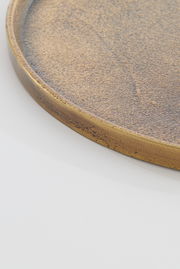 Nahaufnahme einer runden, flachen Schale mit goldener, strukturierter Oberfläche, seitliche Perspektive.