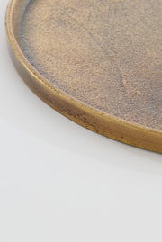 Nahaufnahme einer runden, flachen Schale mit goldener, strukturierter Oberfläche, seitliche Perspektive.