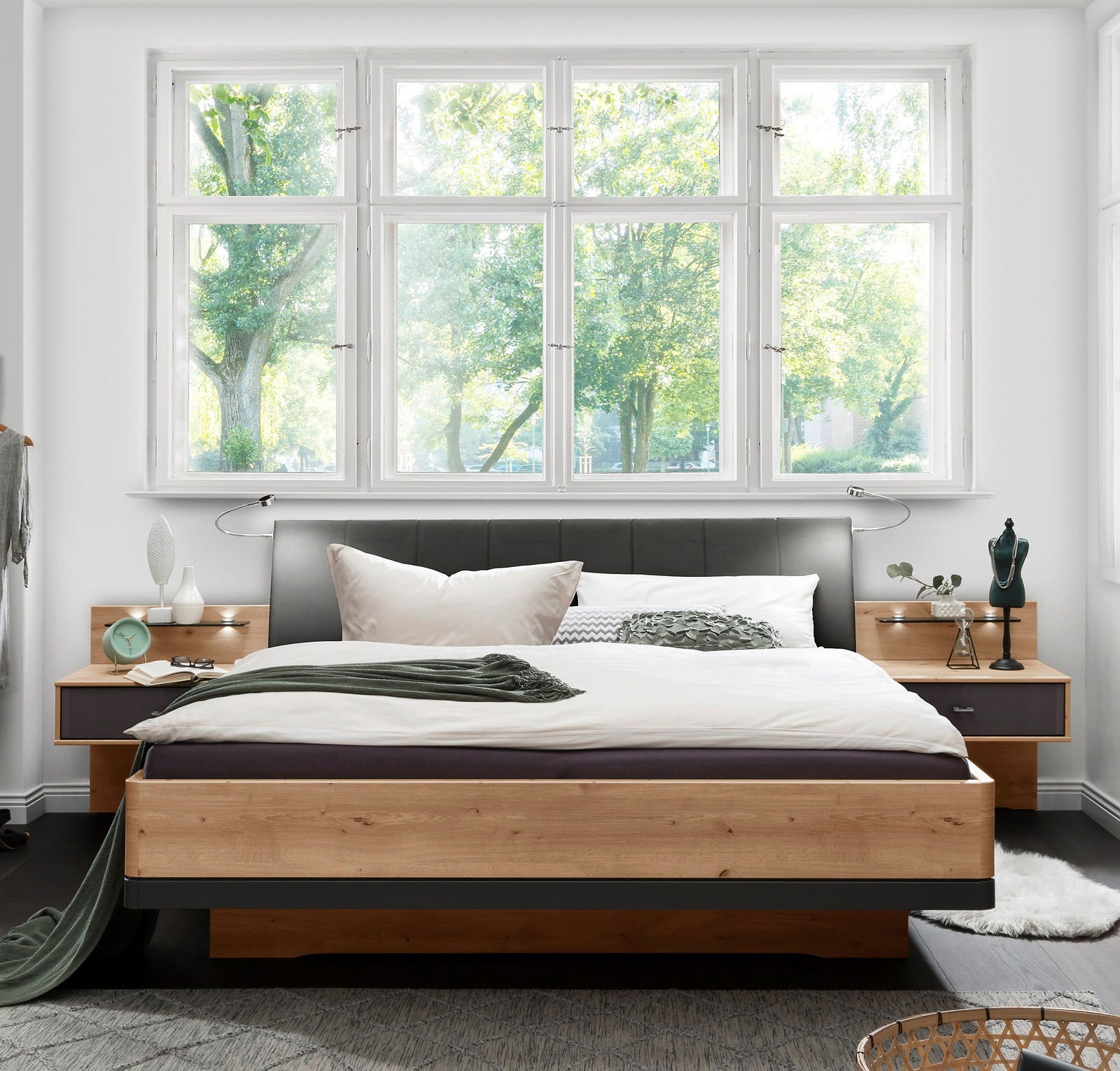 Modernes Futonbett aus Holz mit gepolstertem Kopfteil, umgeben von Nachttischen, in einem hellen Raum mit großen Fenstern, Vorderansicht