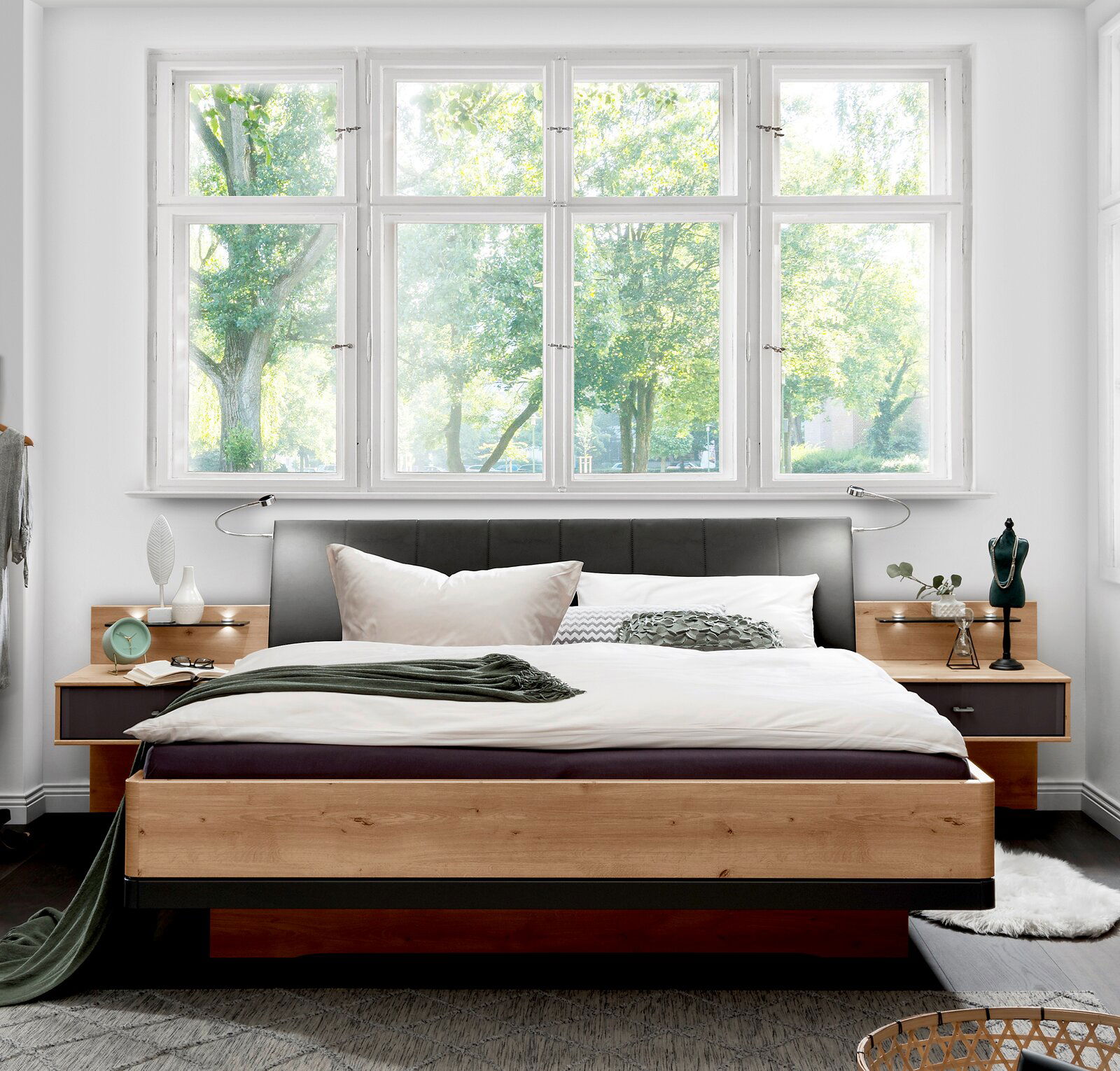 Modernes Futonbett aus Holz mit gepolstertem Kopfteil, umgeben von Nachttischen, in einem hellen Raum mit großen Fenstern, Vorderansicht